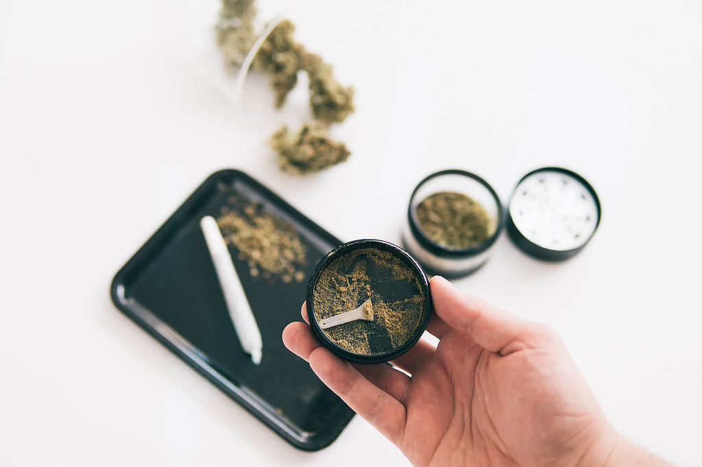 Kief in einem Grinder mit einem Rolling Tray und einem Joint im Hintergrund.